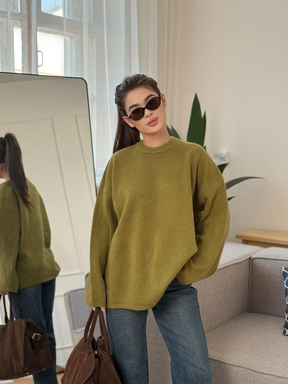 Woman posing in an oversized olive green sweater and blue denim jeans.