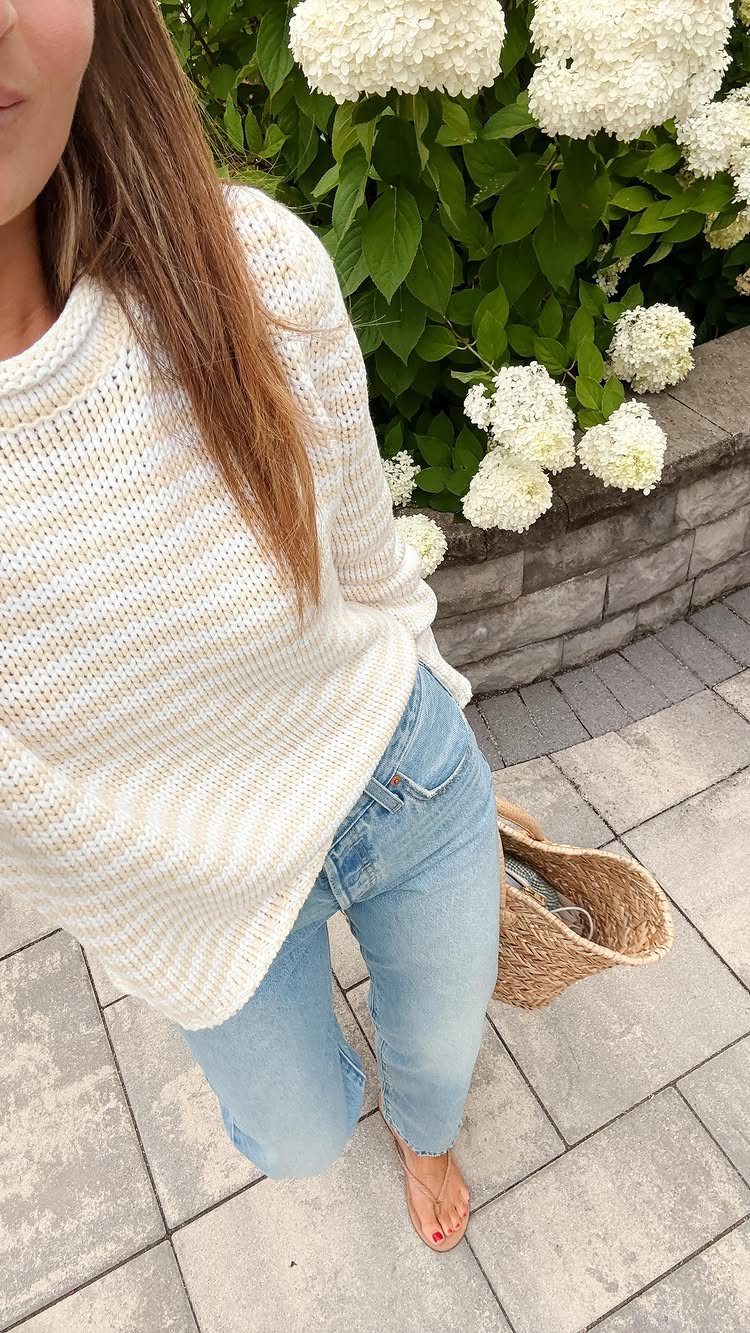 Person wearing a striped knit sweater and light blue jeans standing near white hydrangeas.