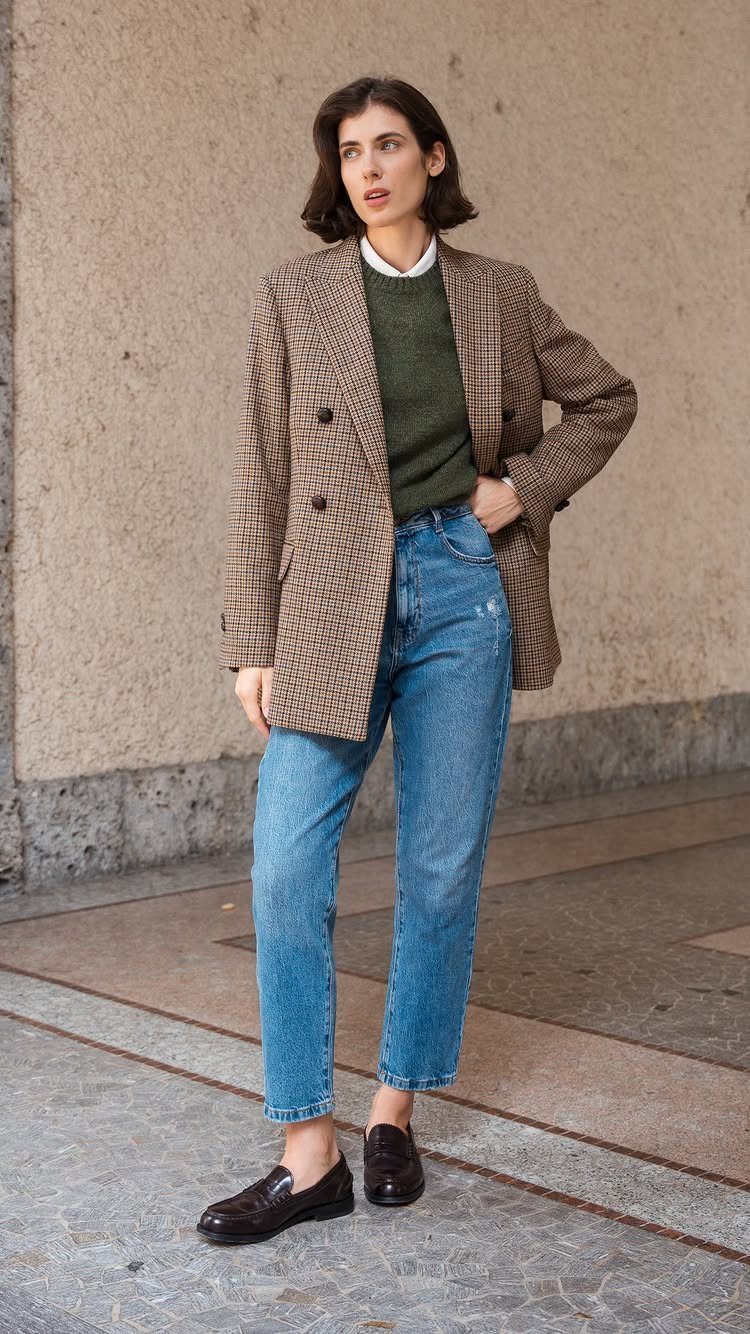 Woman wearing a patterned blazer over a green sweater, white shirt, and blue jeans.