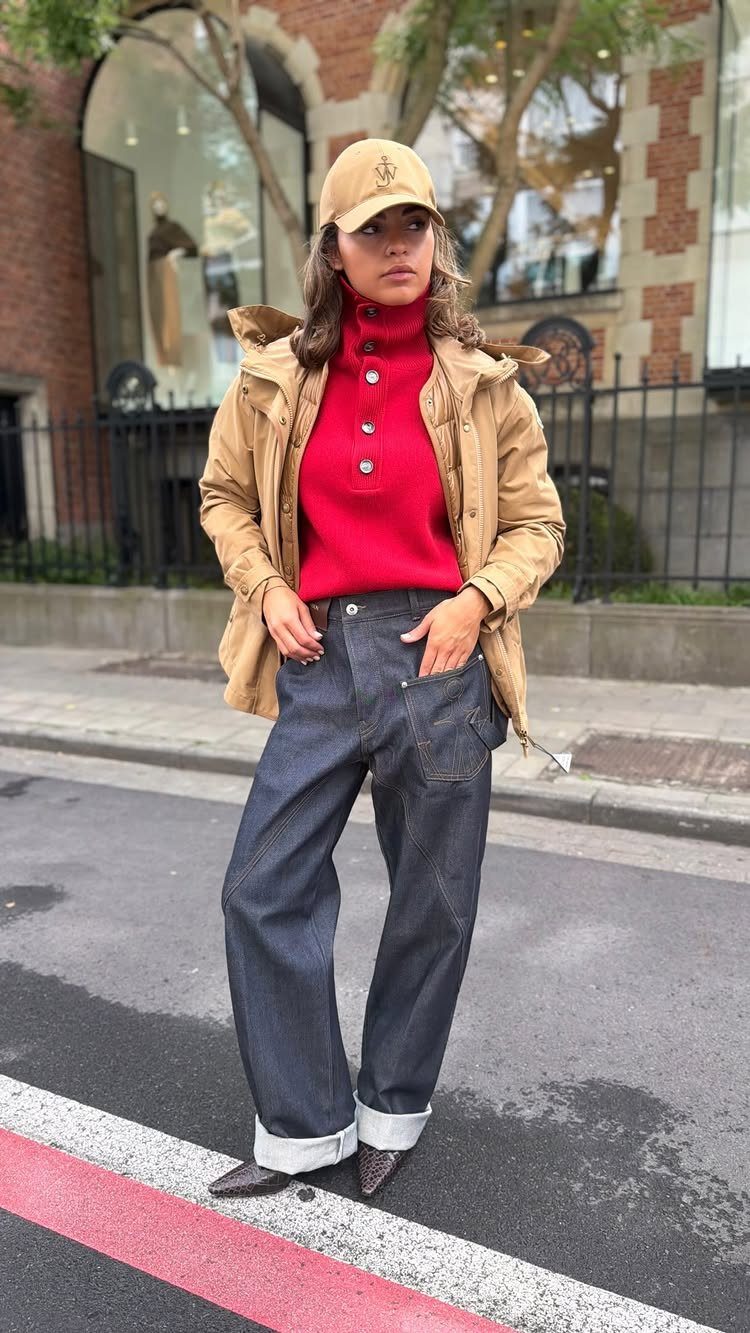 A woman wearing a bright red turtleneck sweater, tan jacket, and dark wide-leg jeans.