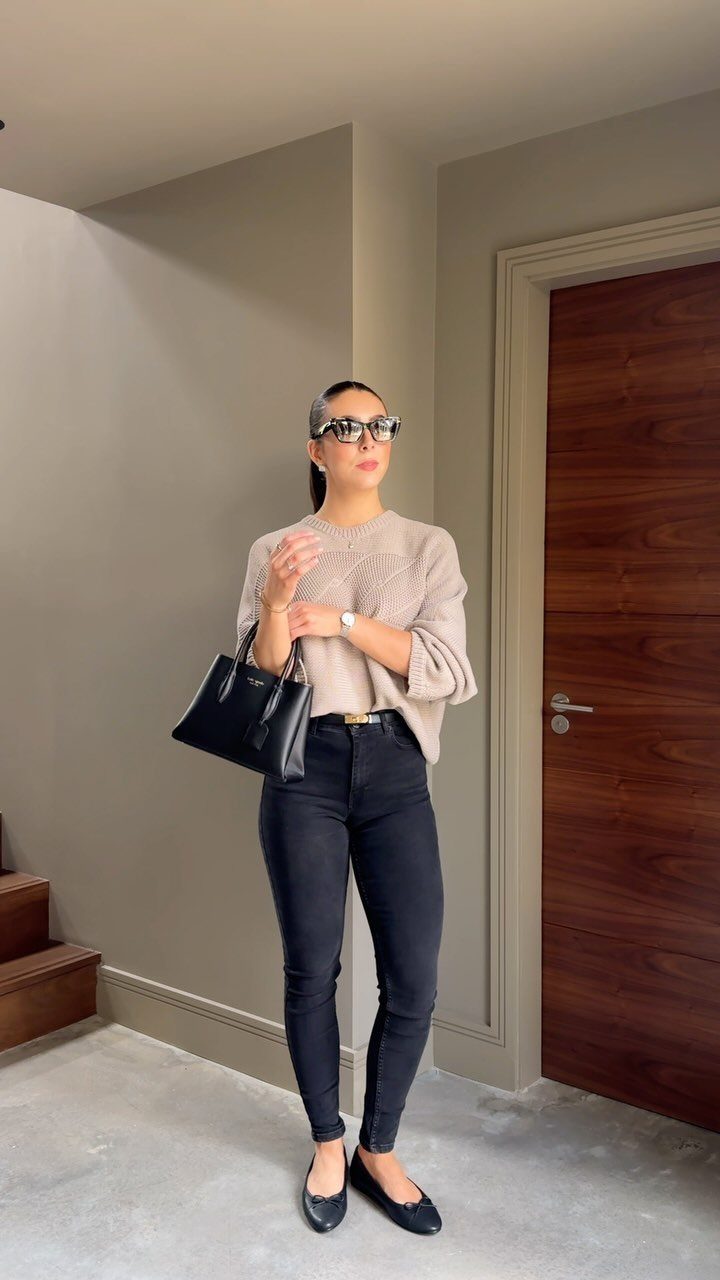 A woman wearing a beige sweater and black jeans standing in a room.