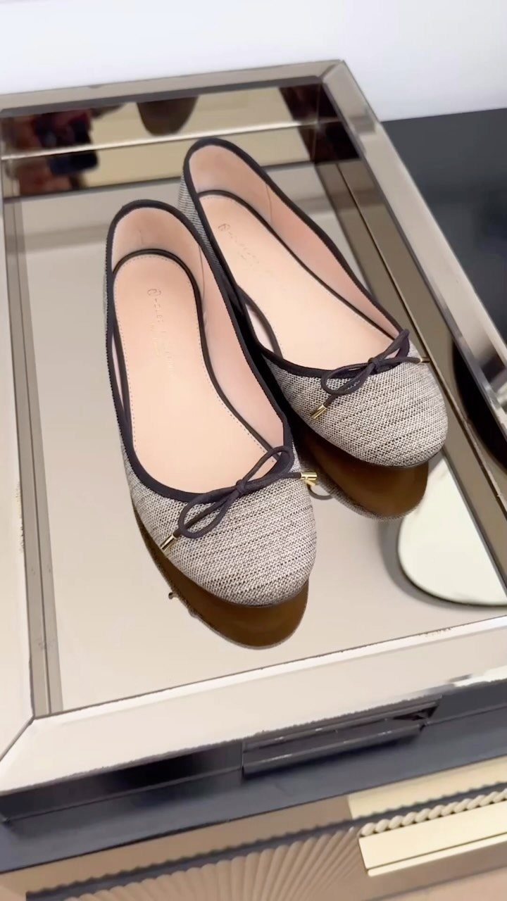 Grey textured ballet flats with black trim sitting on a mirrored tray.