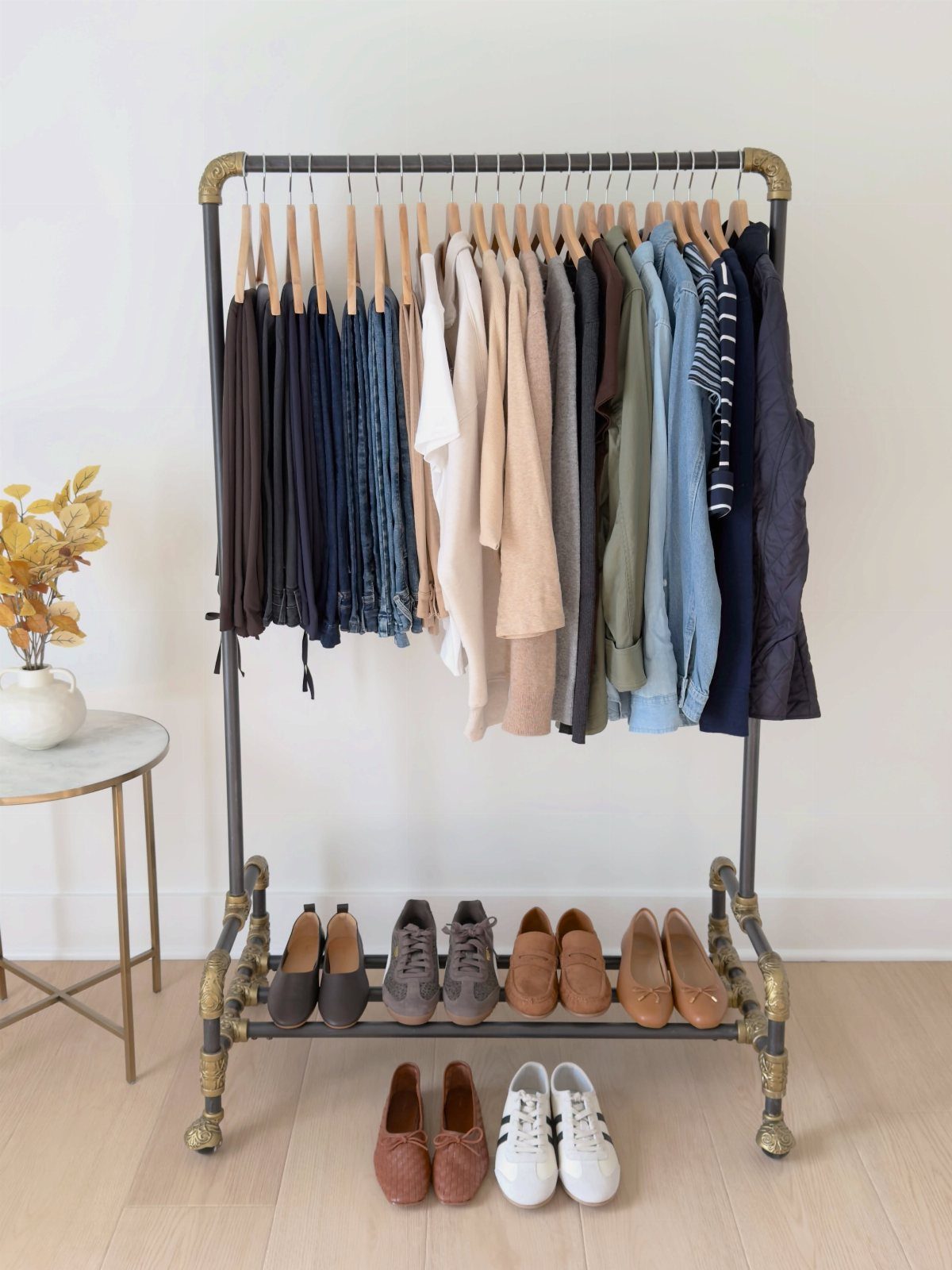A clothing rack filled with neutral-colored garments and several pairs of shoes arranged neatly underneath.