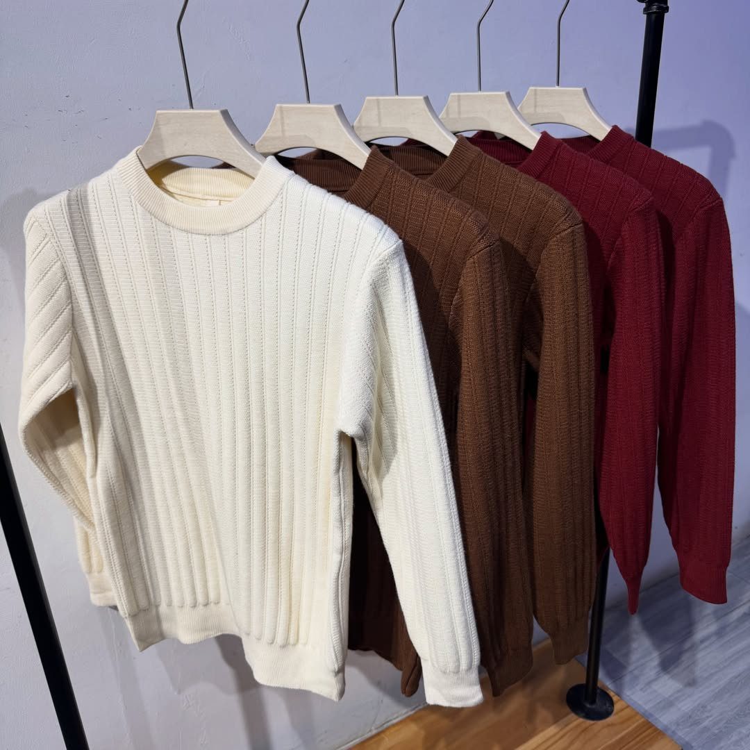 Four ribbed knit sweaters in cream, brown, and red hanging on a clothing rack.