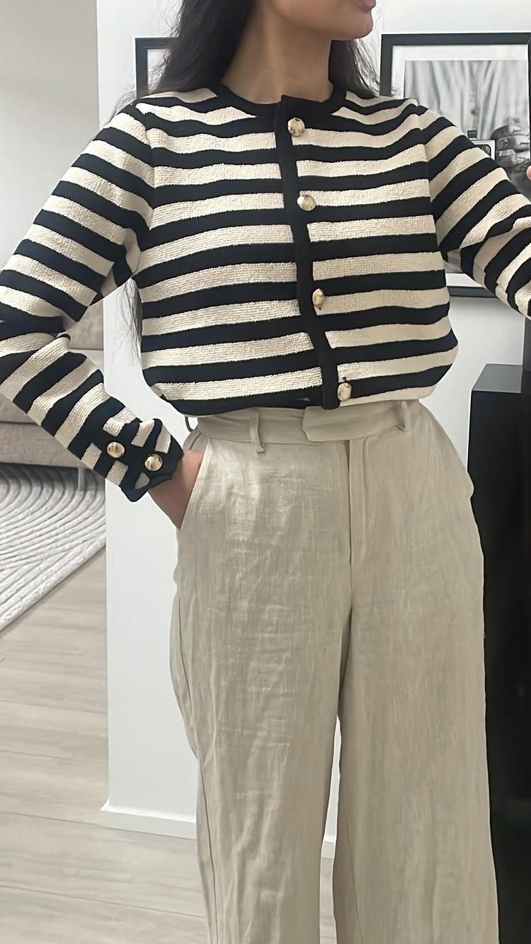 Woman wearing a striped cardigan and beige linen trousers standing in a bright room.
