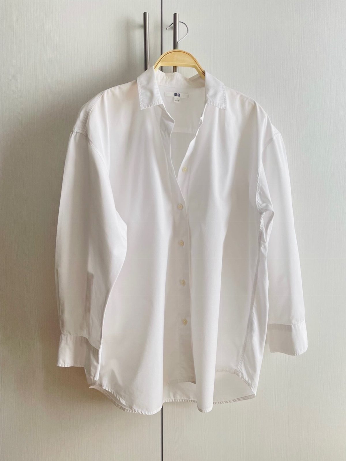 A white long-sleeved button-down shirt hanging on a wooden hanger against a white door.