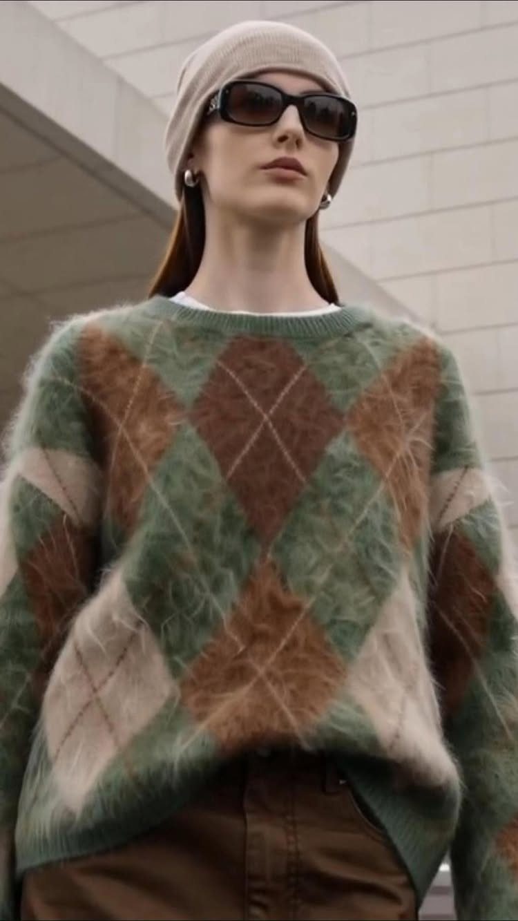 A person wearing a fuzzy green and brown argyle knit sweater and a beige beanie.