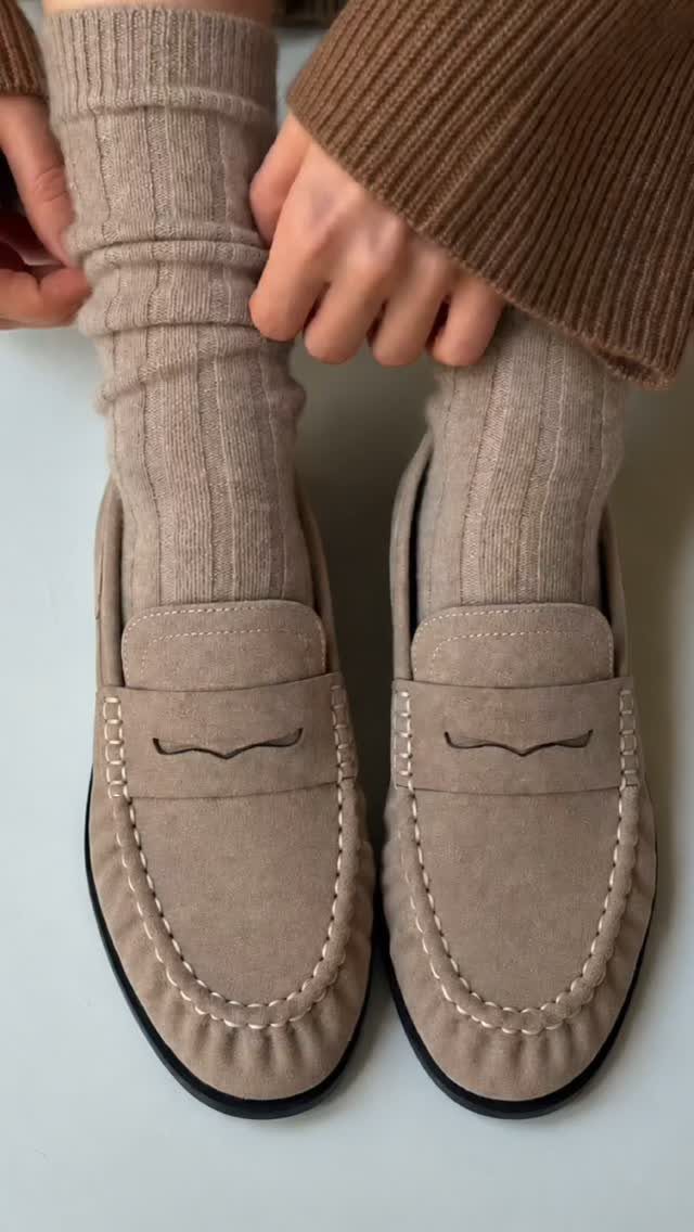Beige suede loafers paired with thick ribbed knit socks on a light background.