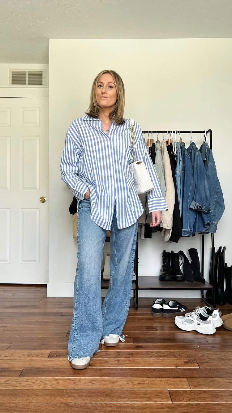 A woman posing in a striped button-down shirt and wide-leg blue jeans.