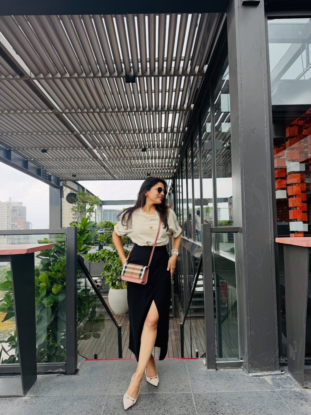 Woman in a beige t-shirt and long black flowy skirt standing on a balcony.