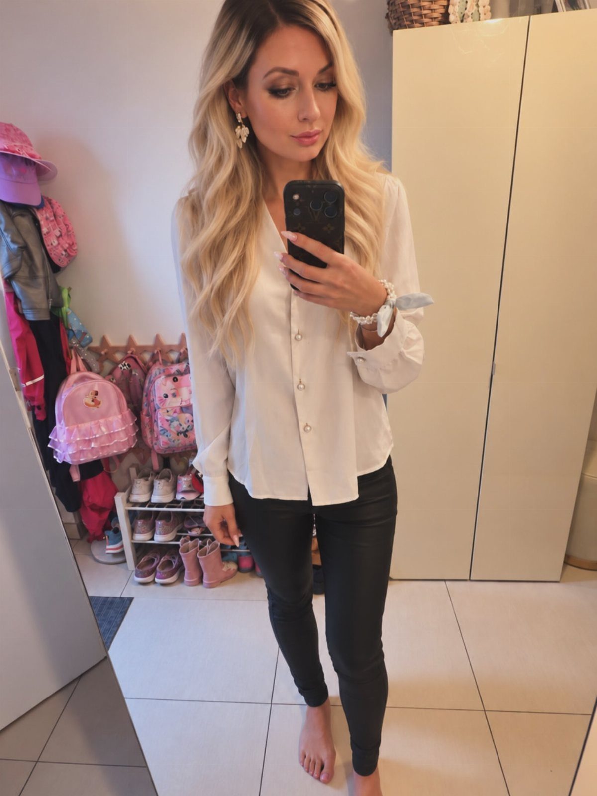 Blonde woman posing in a white button-down shirt and black pants for a mirror selfie.