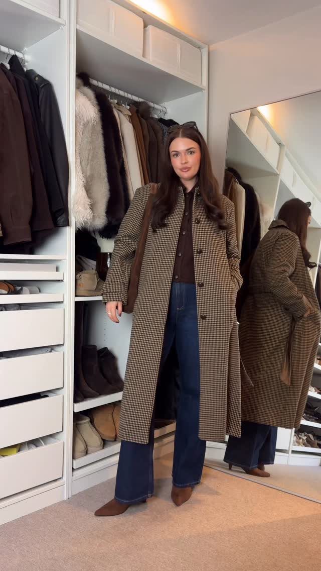 Woman wearing a long patterned coat and blue jeans standing in front of a white closet.
