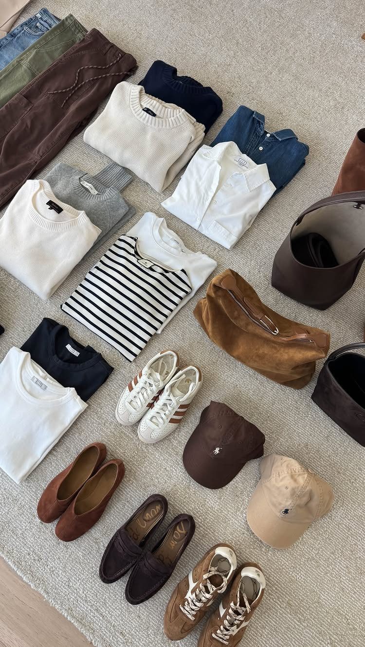 Flat lay of autumn clothing items including sweaters, trousers, loafers, and accessories on a neutral floor.