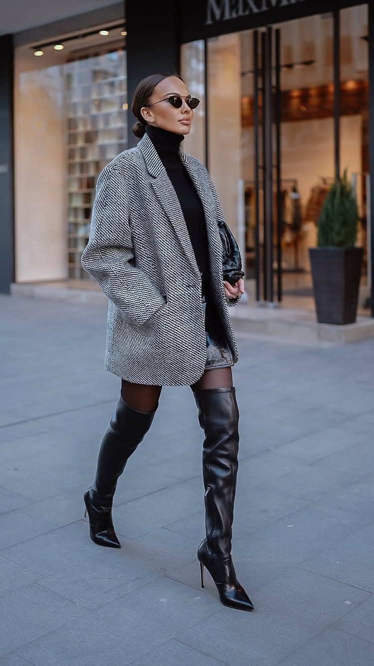 Woman walking in a black turtleneck, grey blazer, leather skirt, and thigh-high boots.