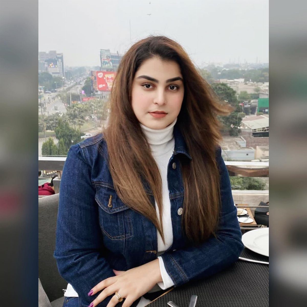 A woman wearing a white turtleneck and a blue denim jacket sitting outdoors.