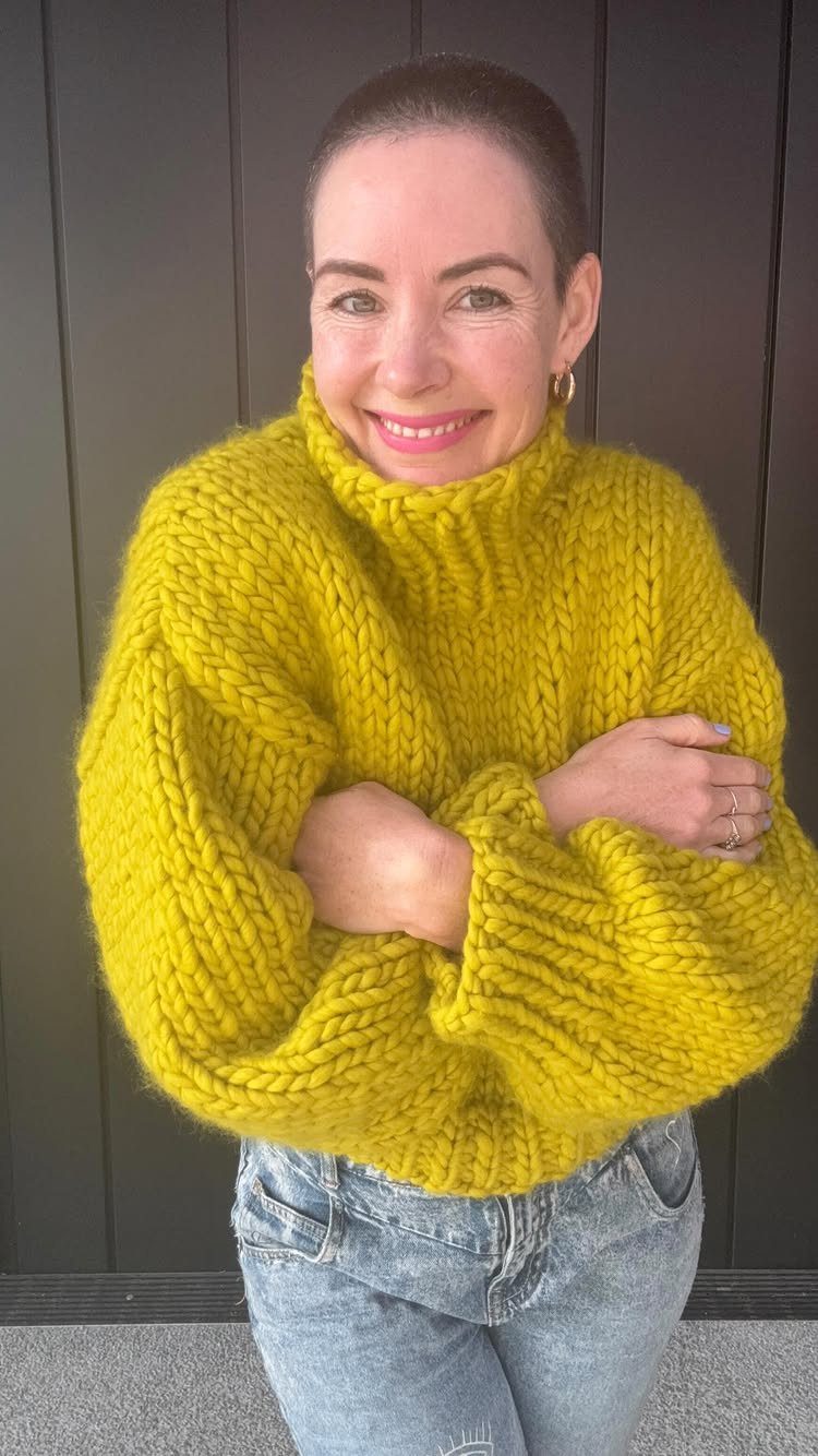 A woman wearing a chunky yellow knit turtleneck sweater and light blue denim jeans.