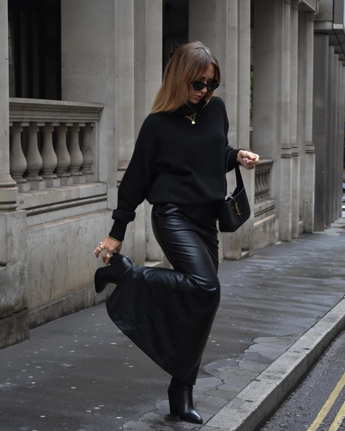Woman walking on a city sidewalk wearing a black turtleneck and long leather skirt.