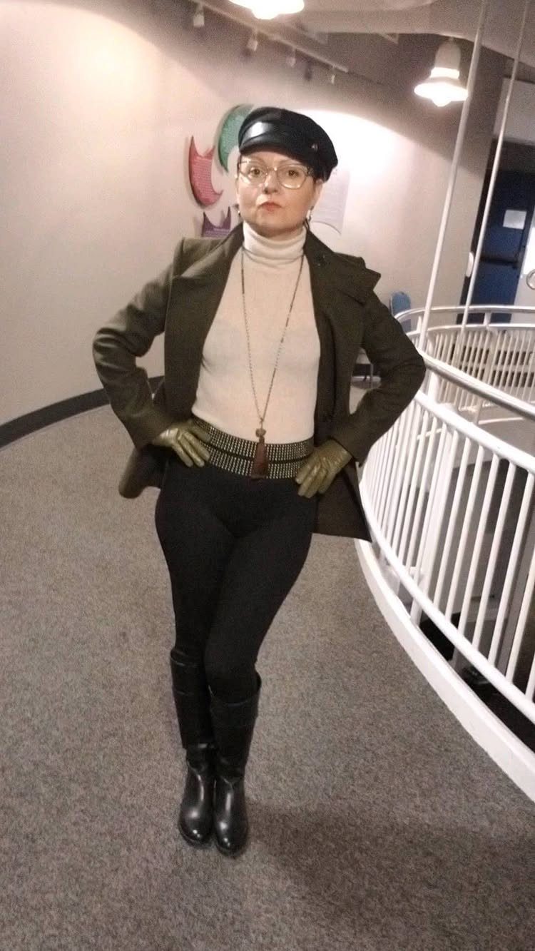Woman wearing a white turtleneck under an olive green structured blazer and black leggings.