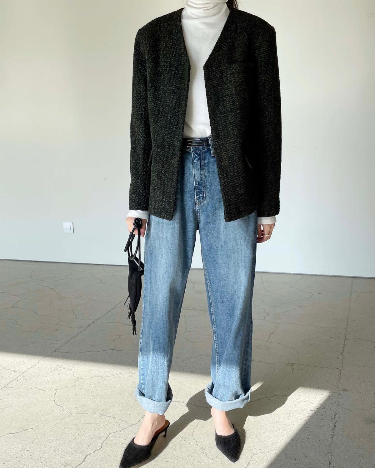 Person wearing a white turtleneck, dark tweed jacket, and blue jeans with black mules.