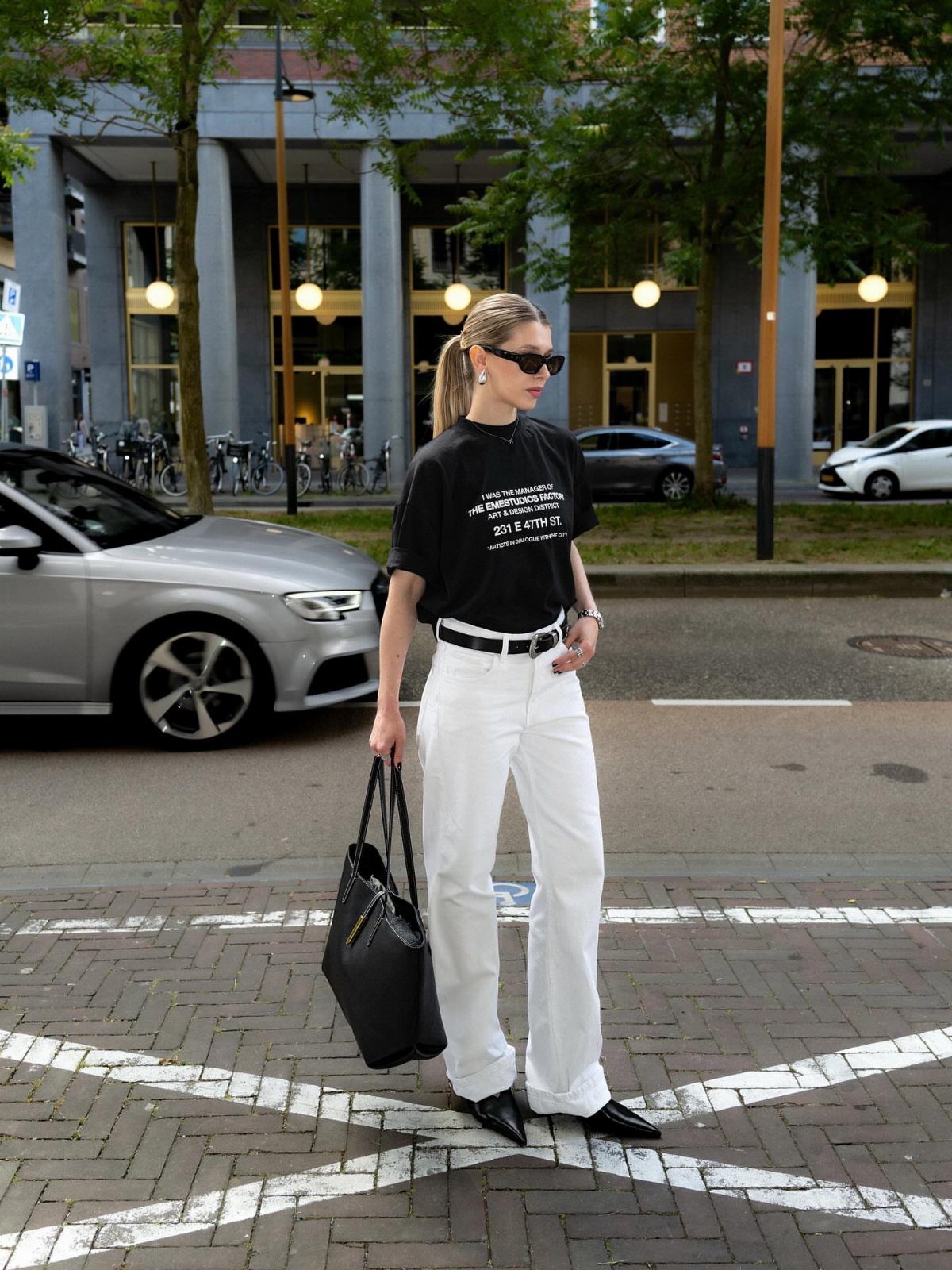 A woman wearing white jeans and a black graphic t-shirt standing on a city street.