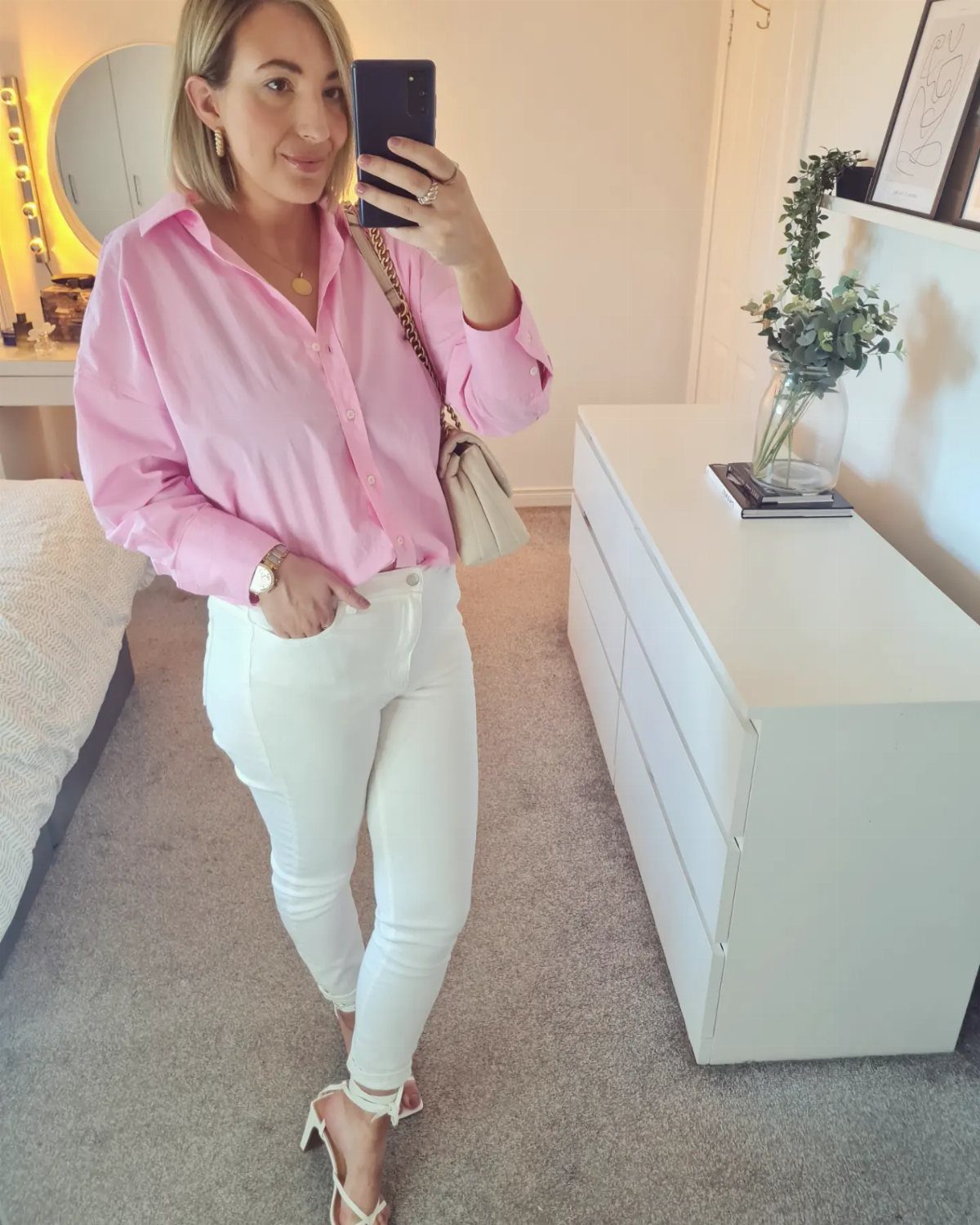 Woman posing in a pink button-down shirt and white jeans with white sandals.