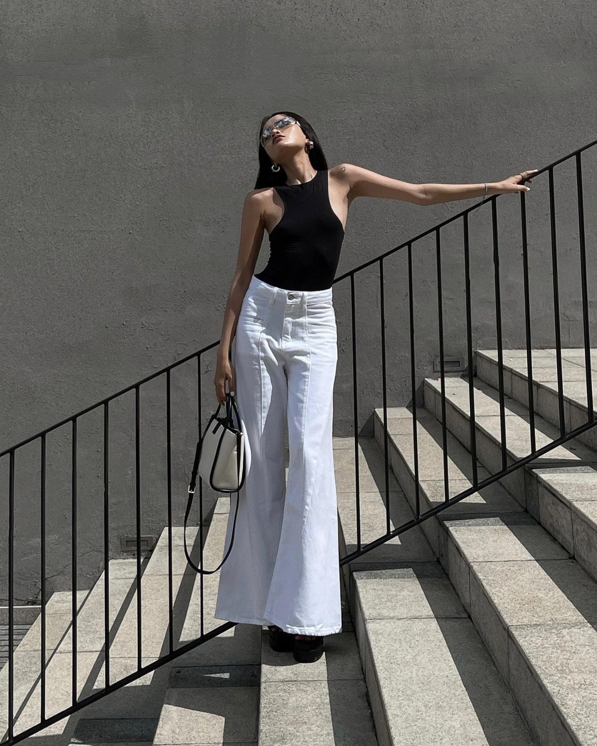 Woman in a black tank top and wide-leg white jeans posing on concrete stairs.