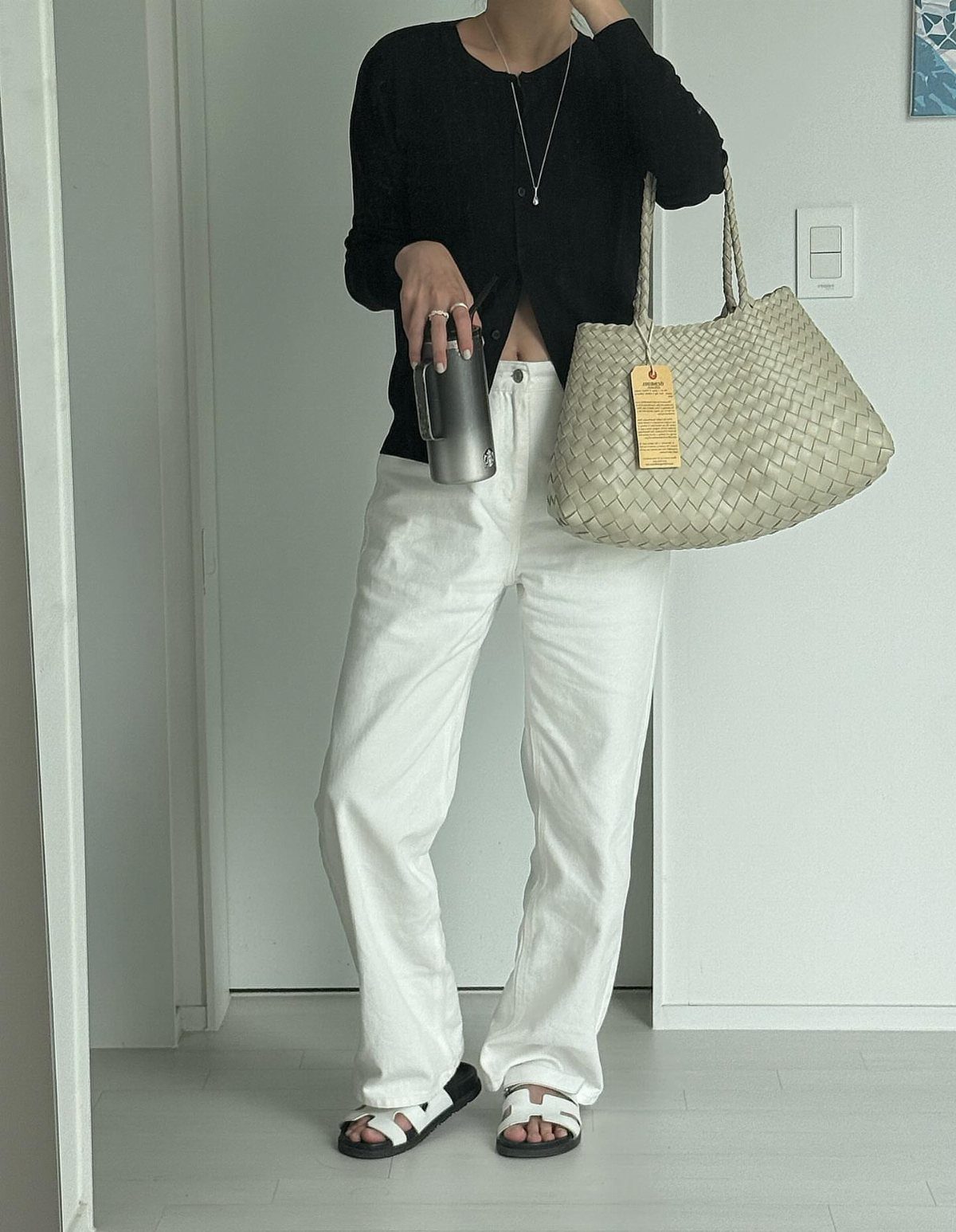 Person in white jeans and black top carrying a large woven tote bag.