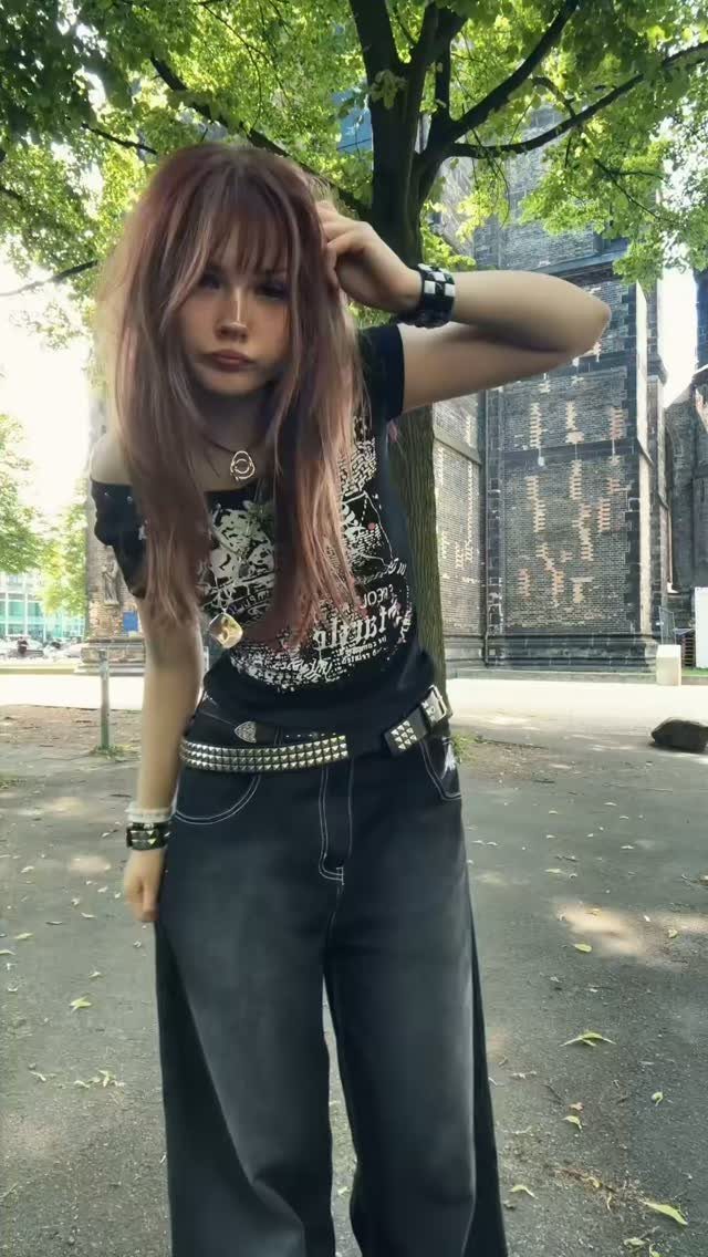 A young woman posing in black wide-leg jeans and a graphic t-shirt outdoors.