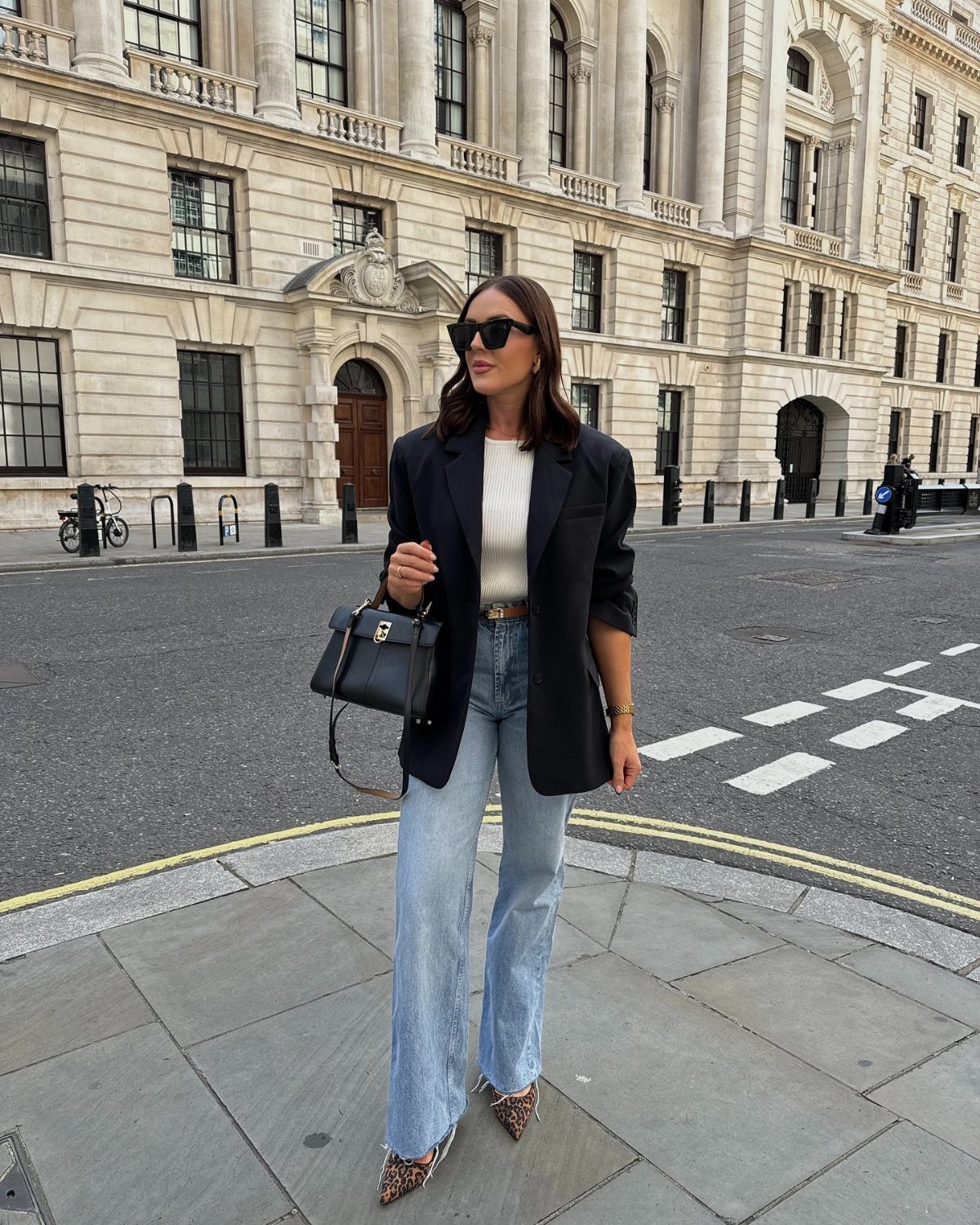 Woman wearing a black oversized blazer, white top, and light blue wide leg jeans outdoors.
