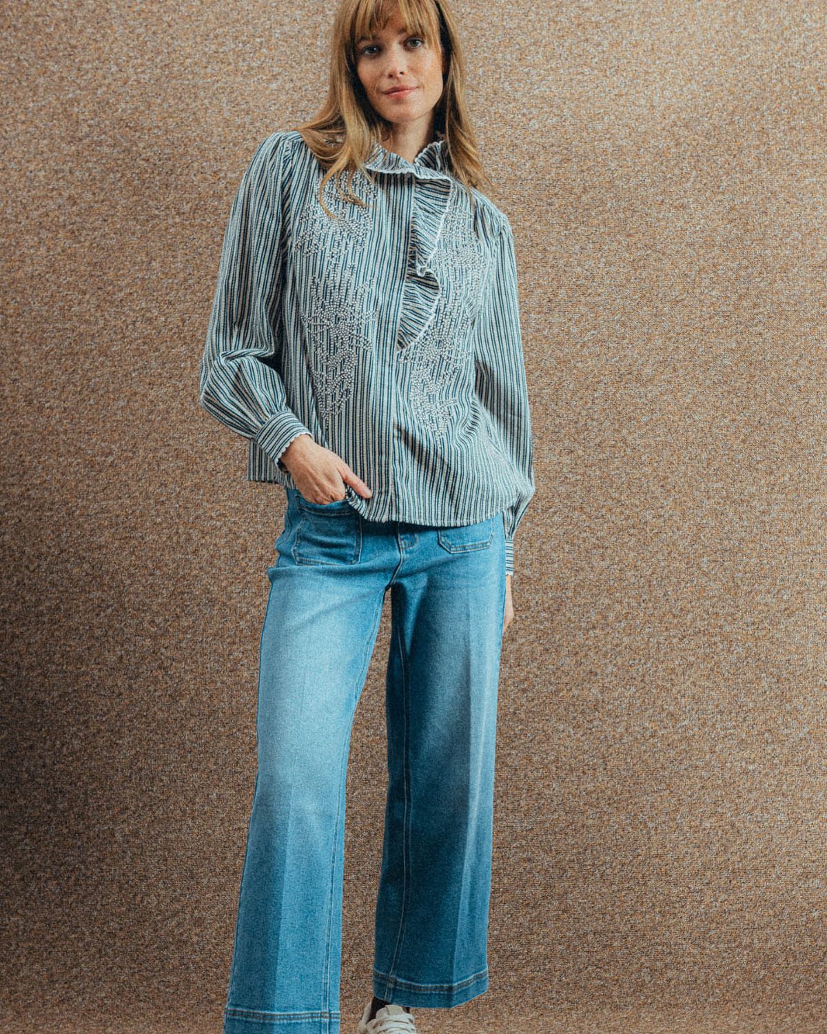 Woman wearing a striped ruffle blouse and light blue wide leg denim jeans.
