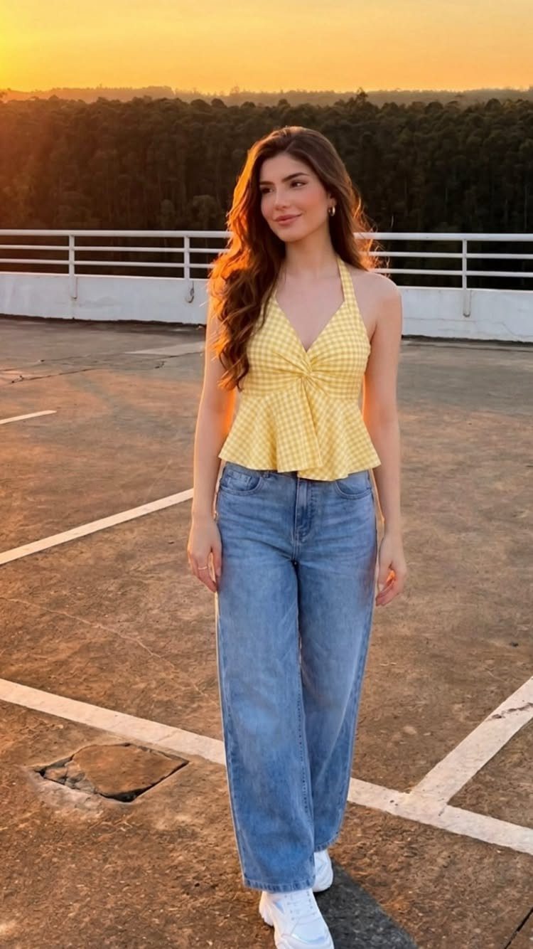 Woman wearing a yellow gingham halter peplum top and blue wide leg jeans at sunset.