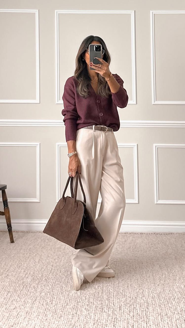 Woman in maroon cardigan and cream wide-leg trousers holding a brown suede handbag.