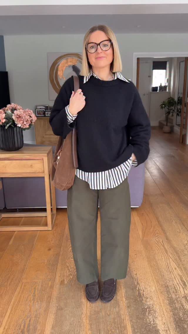 A woman posing in a black sweater, striped shirt, and olive green trousers for a work outfit.