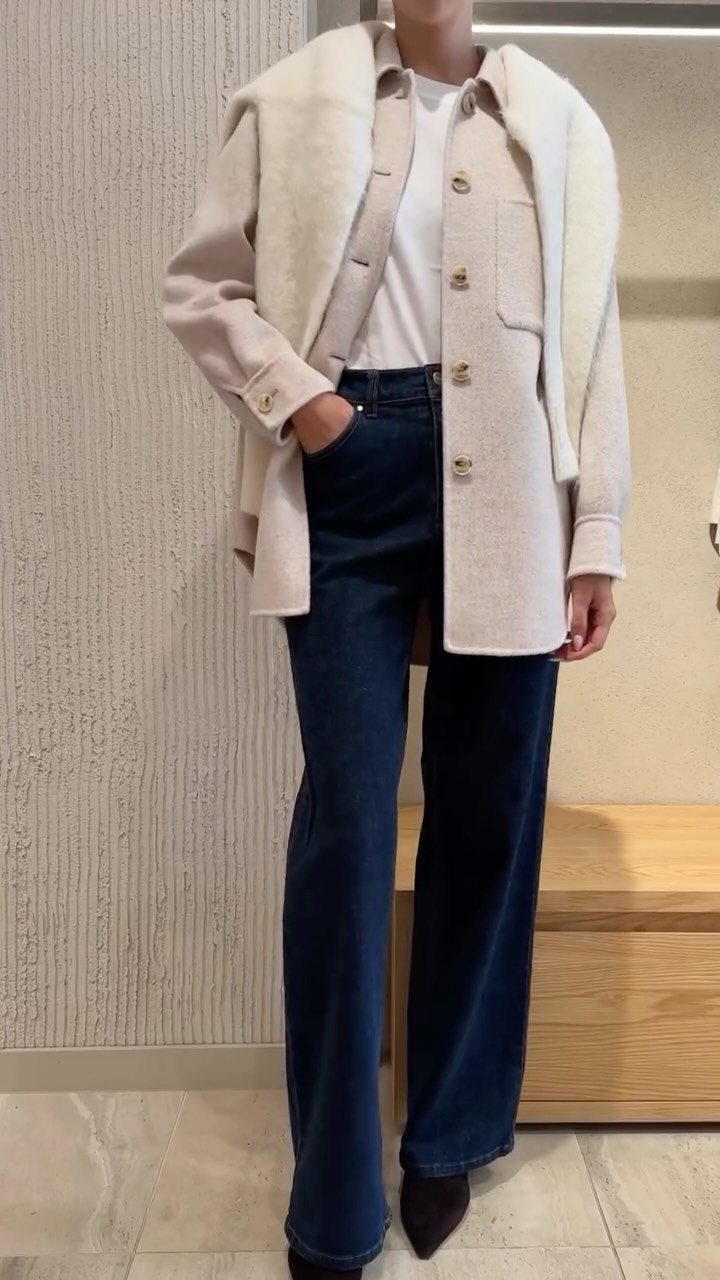 A person wearing a beige wool shacket, white shirt, and dark blue wide-leg jeans.
