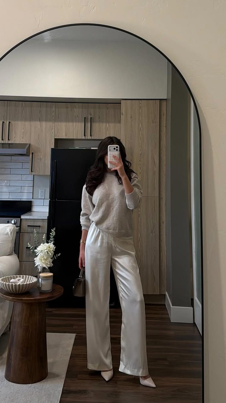 Woman posing in a mirror wearing a beige sweater and wide-leg satin pants.
