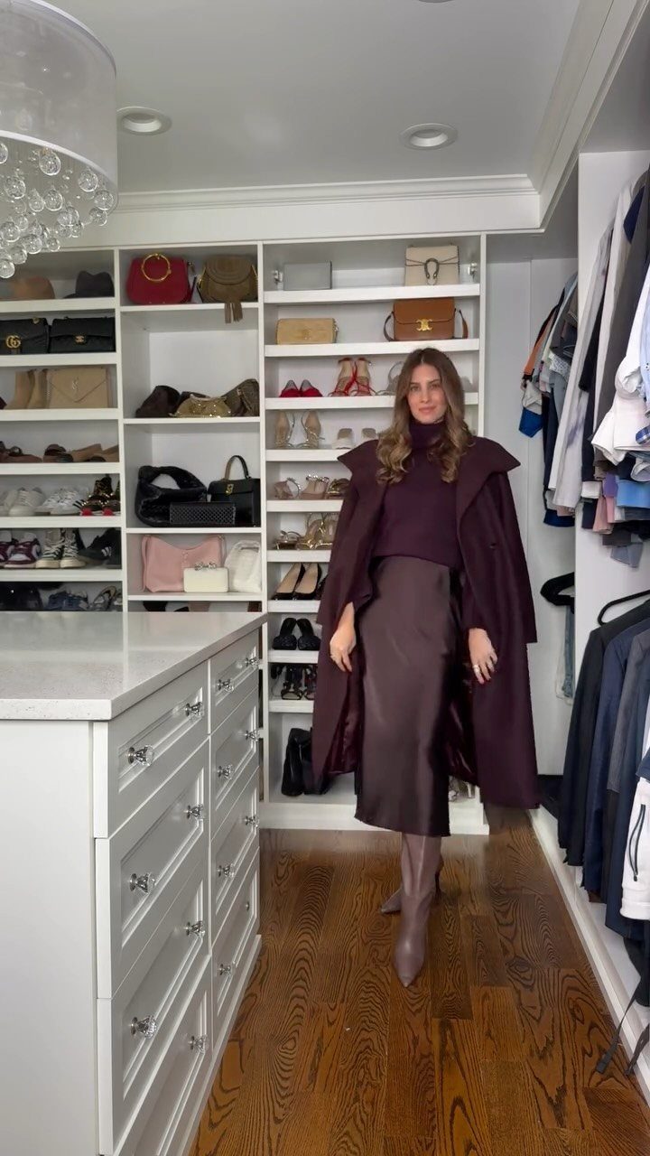 Woman wearing a purple turtleneck, satin midi skirt, and long coat in a closet.