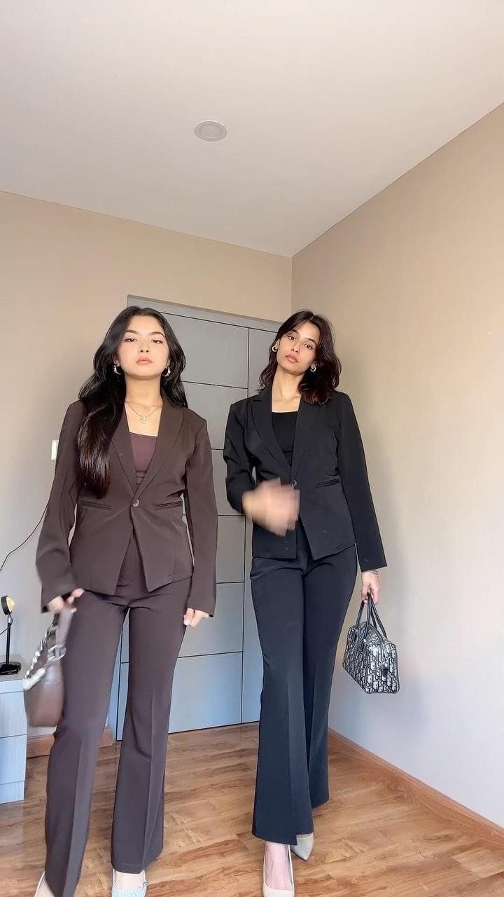 Two women posing in stylish brown and black tailored blazer pant suits.