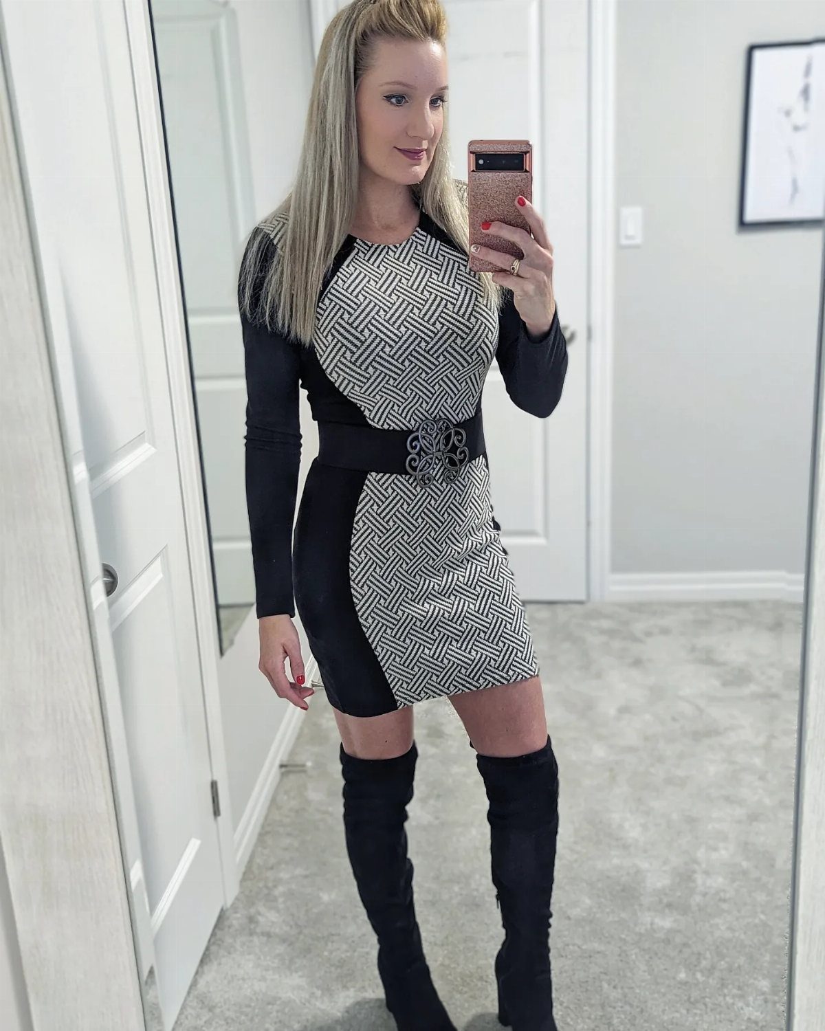 Woman in a patterned black and white mini dress and black thigh-high boots taking a selfie.