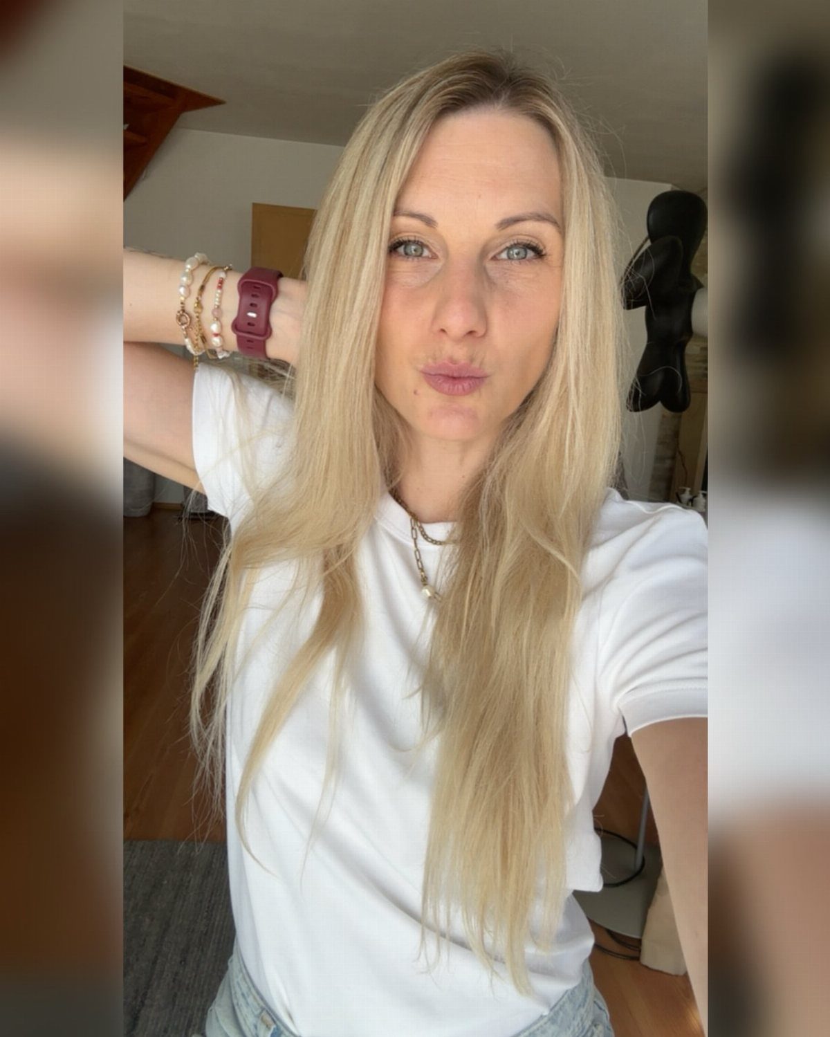 A blonde woman wearing a simple white t-shirt and silver necklace posing for a selfie.