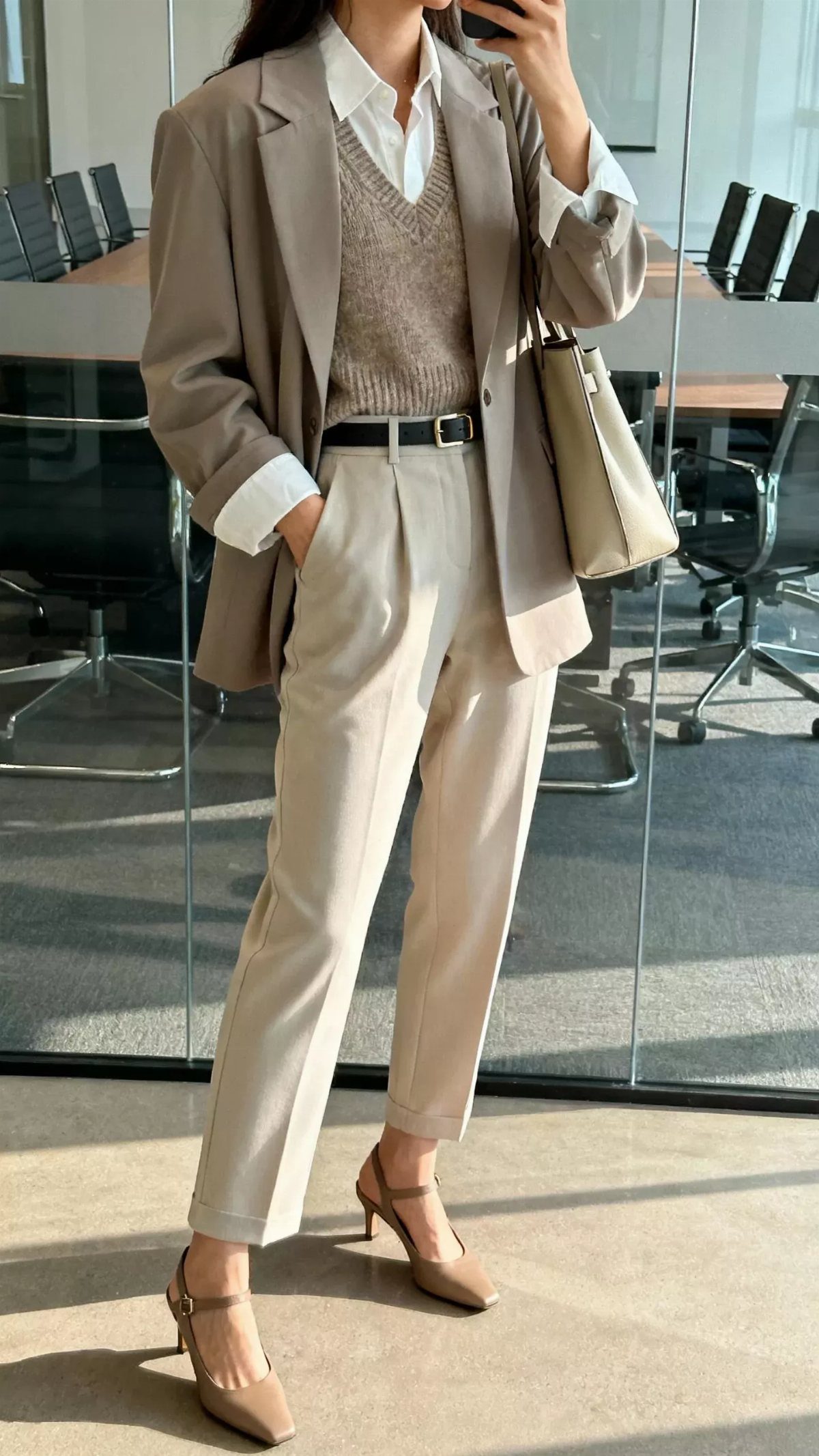 Woman wearing a beige blazer, knit vest, and cream trousers in a modern office.