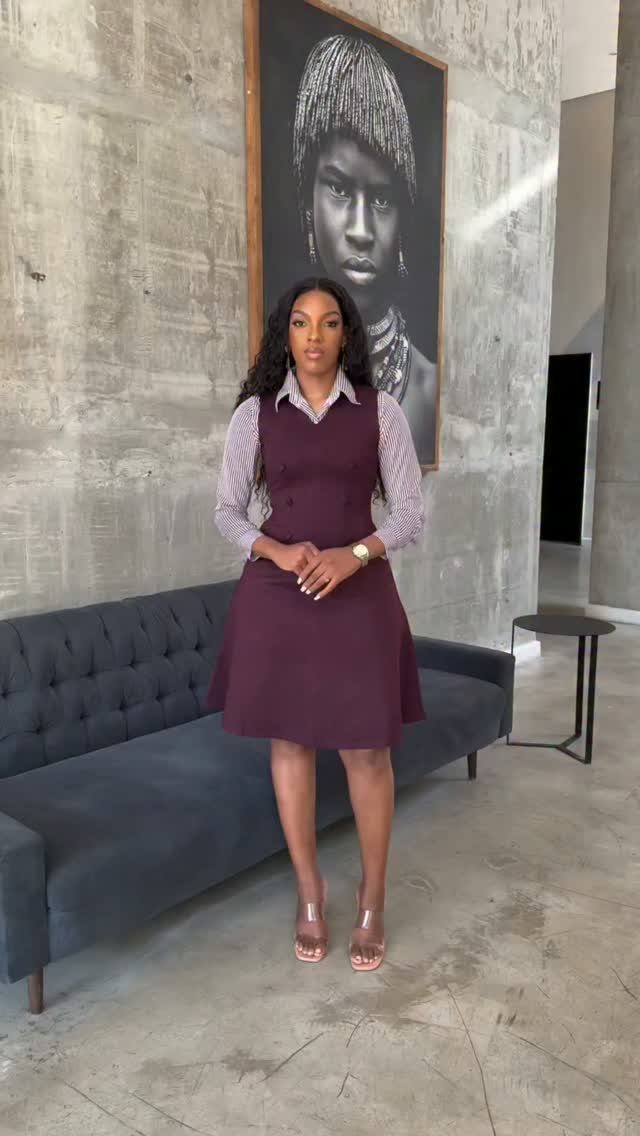 A woman posing in a maroon sleeveless dress over a patterned blouse and nude heels.