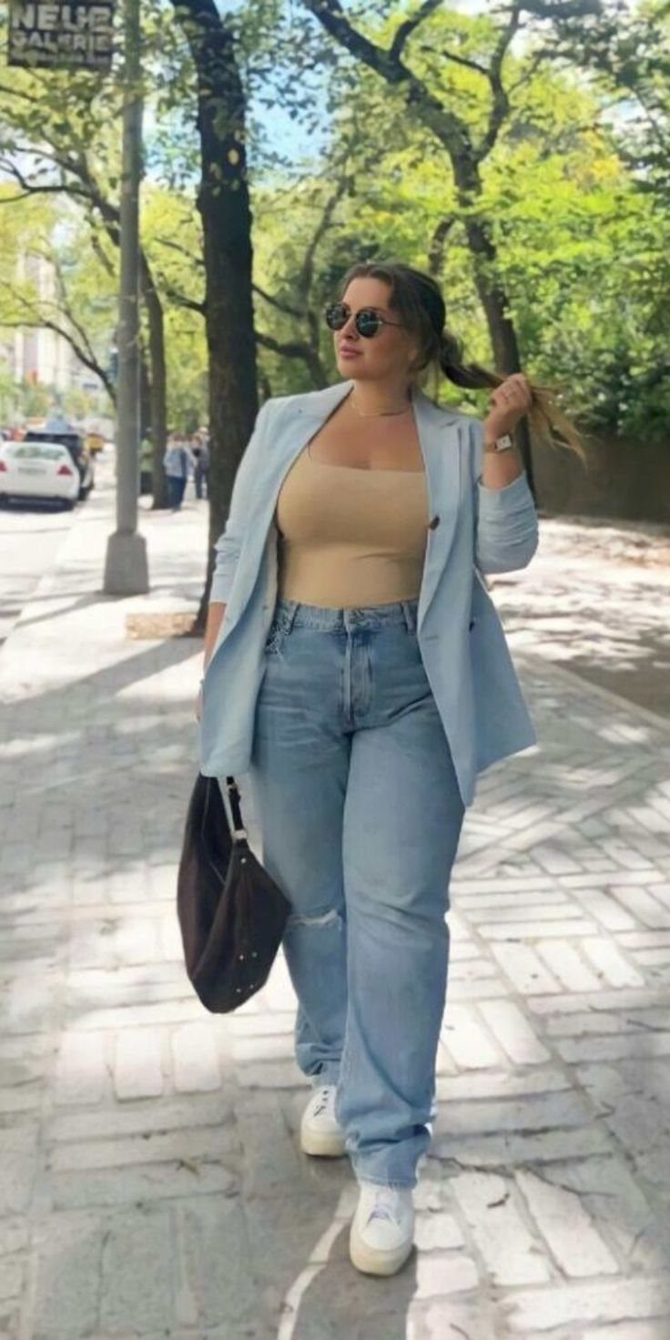 A woman in light blue denim jeans, a tan top, and a blue blazer walking outdoors.