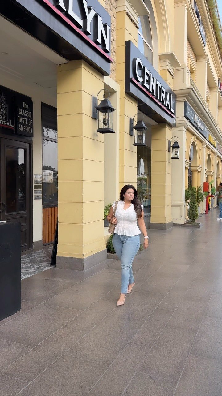 A woman wearing a white peplum blouse and light blue jeans walking on a city sidewalk.